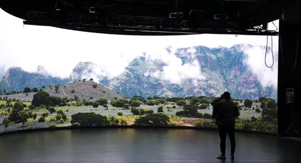 Person standing before a curved LED volume displaying a misty mountain landscape, lit only by the screen
