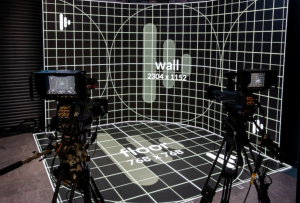 Two broadcast cameras facing a curved LED wall and LED floor displaying calibration grid patterns labelled wall 2304 x 1152 and floor 768 x 768
