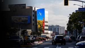 Curved architectural LED billboard on a building above Sunset Boulevard showing a fashion advertisement, with traffic passing below