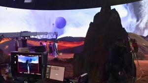 Film crew working at monitors inside a curved LED volume displaying a rocky alien landscape with a purple planet