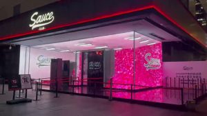 Transparent LED glass display glowing at a retail storefront entrance at night, showing HOLODECK inVIS transparent LED technology