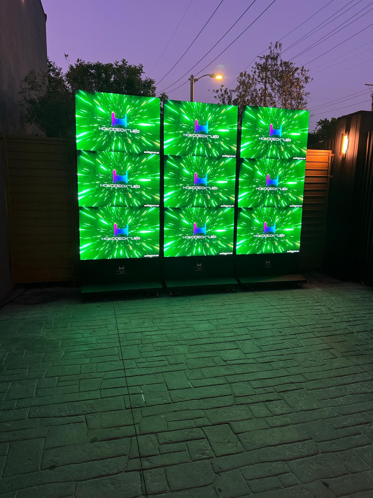 Three HoloTotem LED totem displays outdoors at dusk showing green HOLODECK LED branded content