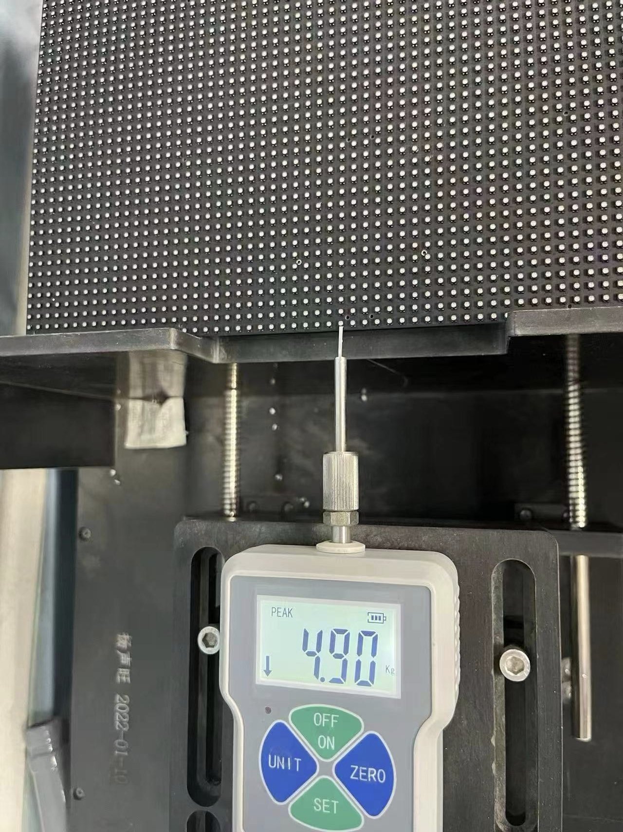 Force gauge reading 4.90 kg pressing against an LED module during a strength test